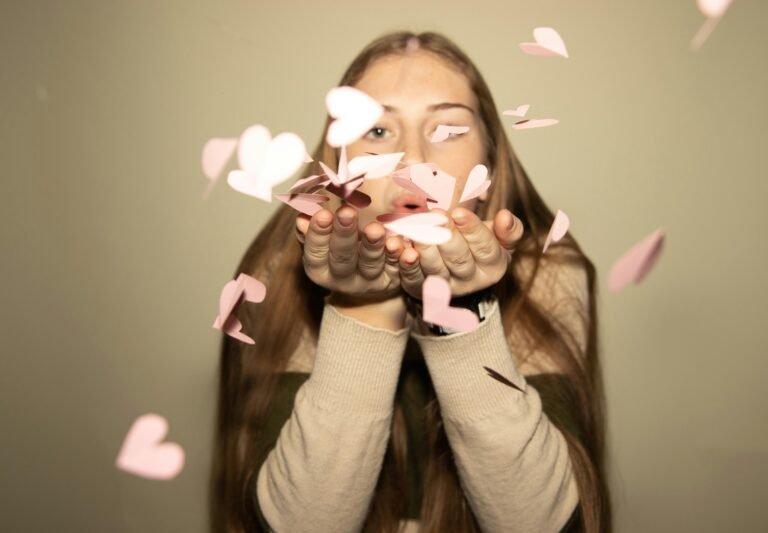 A woman playfully blowing pink heart paper cutouts, capturing a romantic and creative moment.