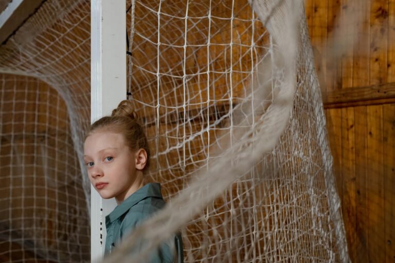A young girl standing by an indoor climbing net, with a thoughtful look.